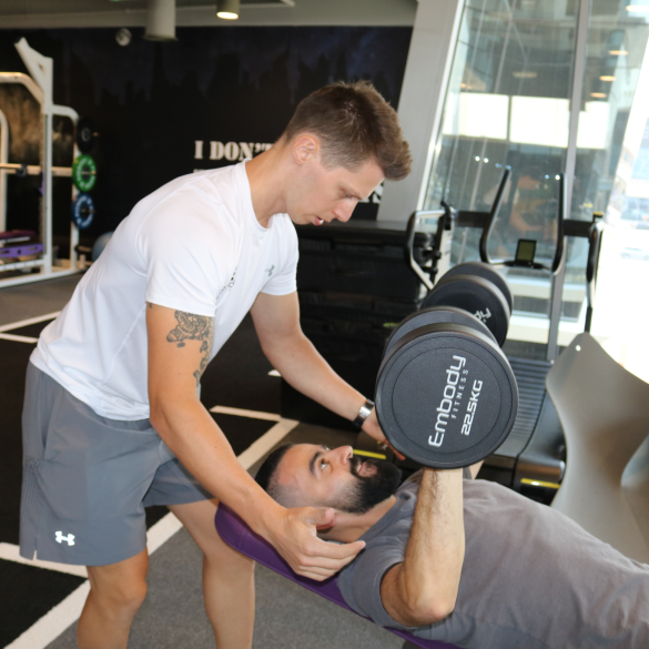 trainer spotting trainee doing dumbbell press
