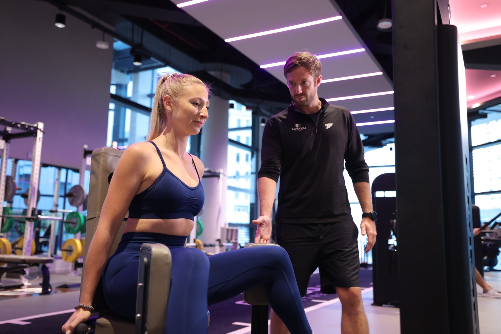 woman member on leg machine with trainer standing up