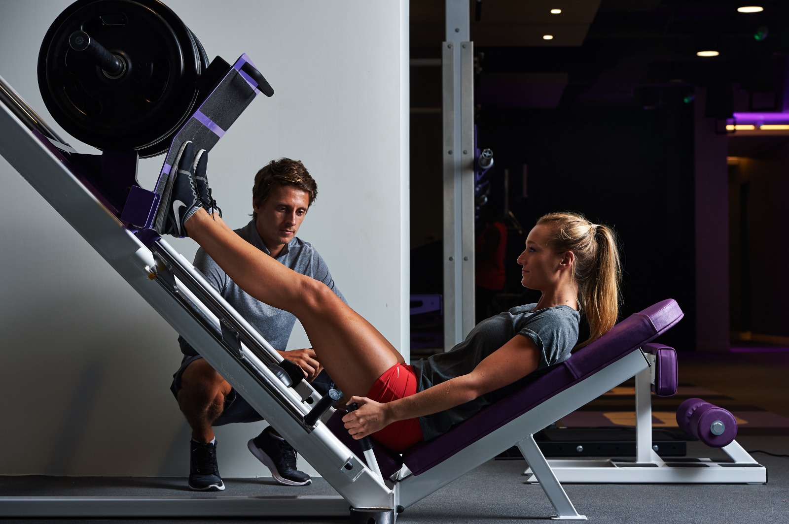 woman doing leg press with trainer watching over